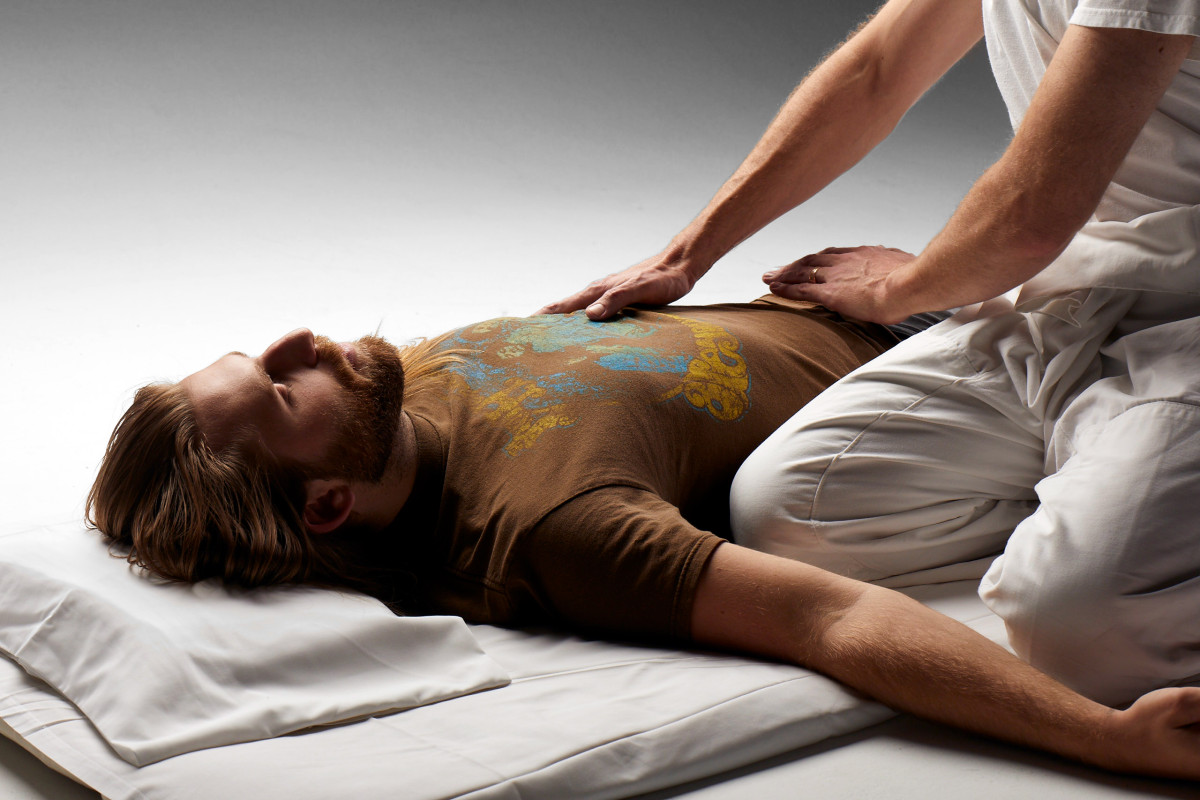 TEAM practitioner Daniel Adler performing hara diagnosis on a female client who is laying on the floor with her arms outstretched.